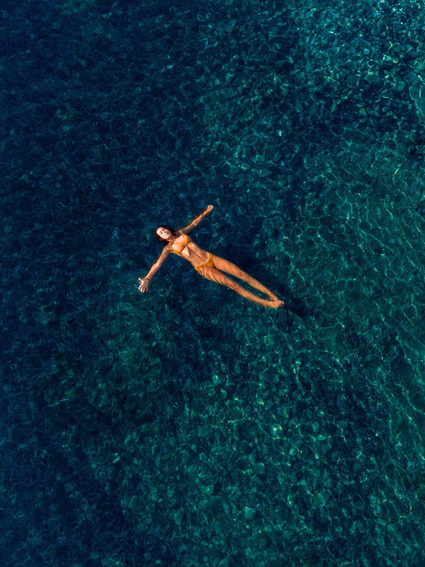 A swimmer floating on her back in clear turquoise water, seen from above